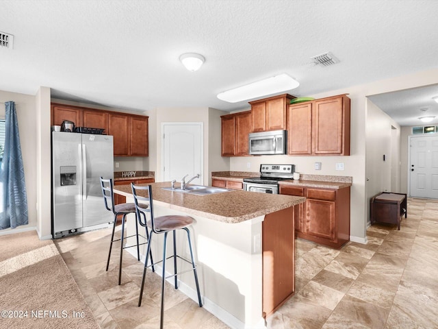 kitchen with an island with sink, a kitchen breakfast bar, a textured ceiling, sink, and stainless steel appliances