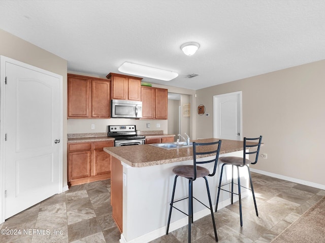 kitchen with a breakfast bar area, a textured ceiling, a kitchen island with sink, sink, and stainless steel appliances