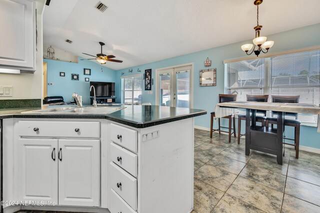 kitchen with sink, ceiling fan with notable chandelier, lofted ceiling, white cabinetry, and hanging light fixtures