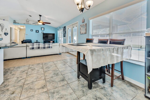 tiled dining room with french doors, ceiling fan with notable chandelier, plenty of natural light, and vaulted ceiling