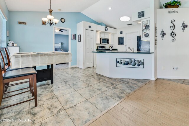 kitchen featuring vaulted ceiling, white cabinets, pendant lighting, stainless steel appliances, and light hardwood / wood-style flooring