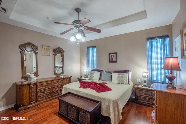 bedroom with a raised ceiling, hardwood / wood-style floors, and ceiling fan