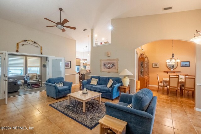 tiled living room featuring ceiling fan with notable chandelier and high vaulted ceiling