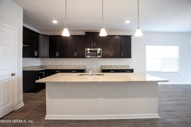 kitchen with light stone countertops, an island with sink, and dark hardwood / wood-style floors