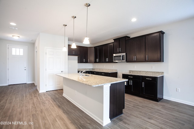 kitchen featuring light stone countertops, pendant lighting, wood-type flooring, a kitchen island with sink, and sink