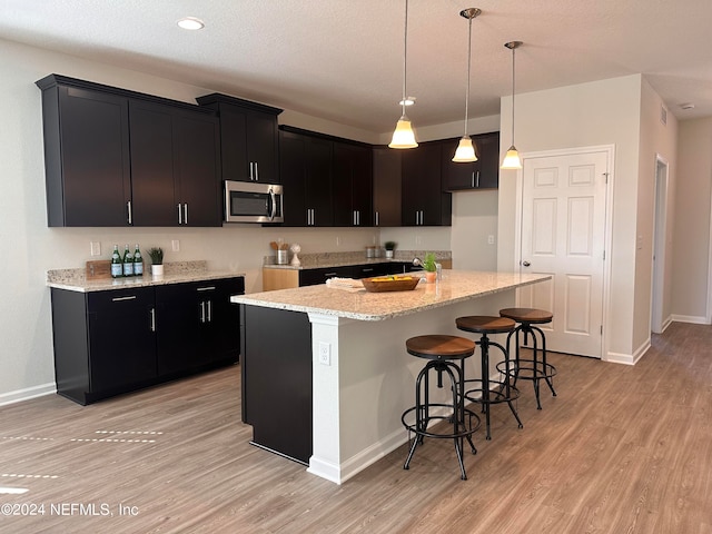 kitchen featuring light stone counters, hanging light fixtures, light hardwood / wood-style flooring, a center island, and a kitchen bar