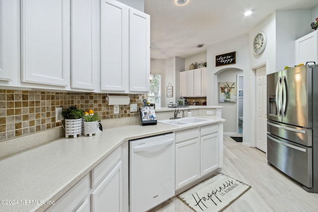 kitchen featuring white dishwasher, stainless steel fridge, sink, and white cabinetry