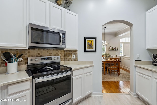 kitchen featuring white cabinets, ornamental molding, appliances with stainless steel finishes, light hardwood / wood-style floors, and decorative backsplash