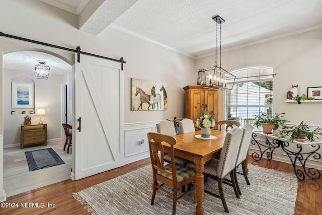 dining space with a barn door, a textured ceiling, an inviting chandelier, and hardwood / wood-style floors