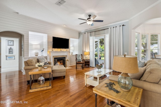 living room featuring a textured ceiling, wooden walls, hardwood / wood-style floors, ornamental molding, and ceiling fan