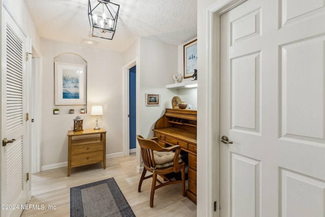 office featuring a notable chandelier, light wood-type flooring, and a textured ceiling