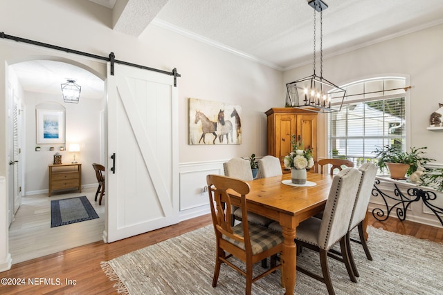 dining room with an inviting chandelier, light wood-type flooring, a textured ceiling, and a barn door