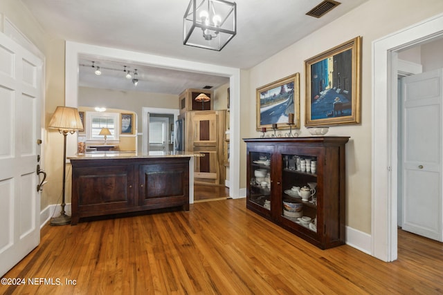 bar featuring a notable chandelier, decorative light fixtures, dark brown cabinets, and wood-type flooring