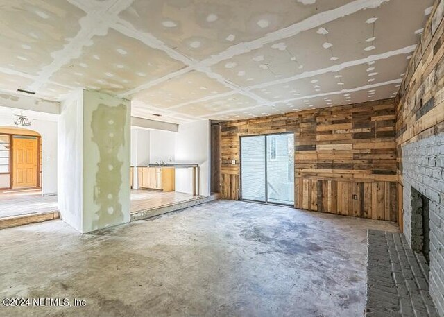 unfurnished living room with wood walls, concrete flooring, and a brick fireplace