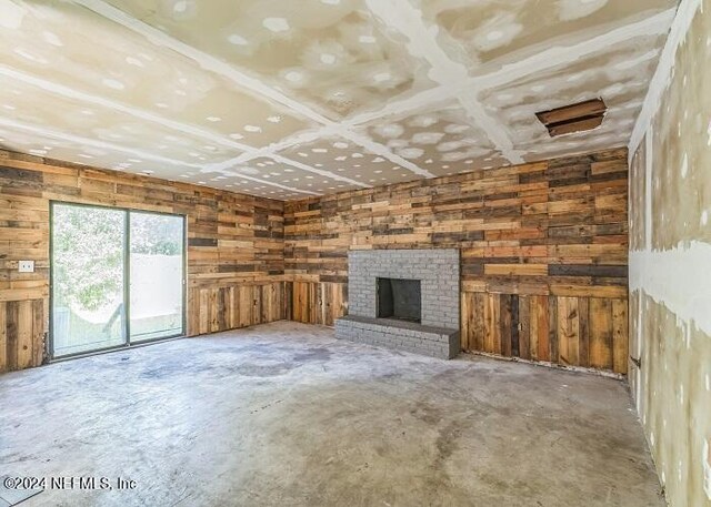 unfurnished living room featuring a fireplace, wood walls, and concrete flooring