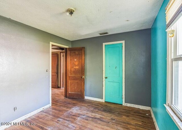 unfurnished bedroom with a textured ceiling, dark hardwood / wood-style floors, and multiple windows