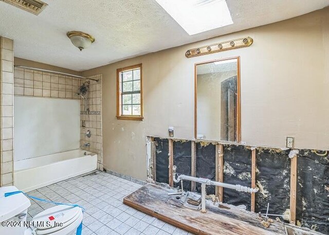 bathroom featuring a skylight, tiled shower / bath combo, tile patterned flooring, a textured ceiling, and toilet