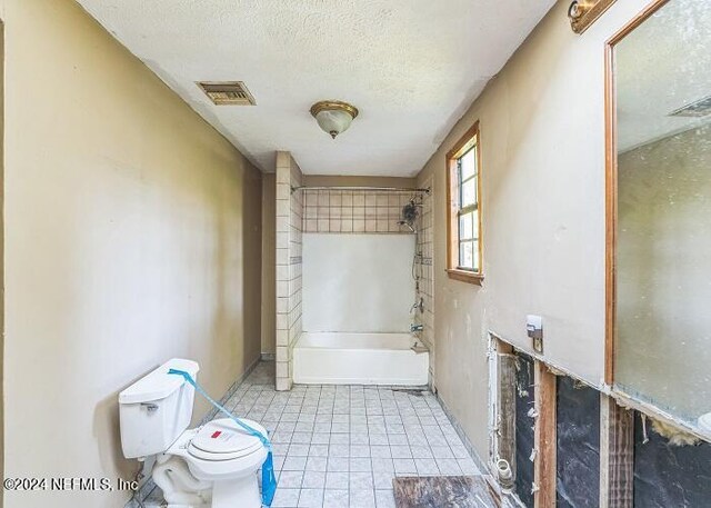 bathroom with a textured ceiling, tiled shower / bath combo, toilet, and tile patterned floors