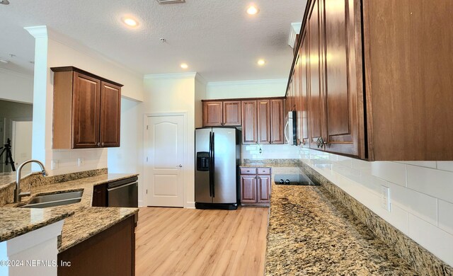 kitchen with a textured ceiling, sink, light hardwood / wood-style flooring, stainless steel appliances, and light stone countertops