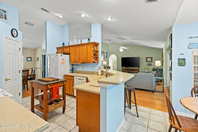 kitchen with white appliances, kitchen peninsula, a kitchen bar, ceiling fan, and sink