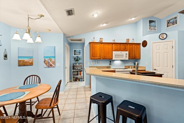 kitchen featuring lofted ceiling, light tile patterned floors, white appliances, decorative light fixtures, and an inviting chandelier