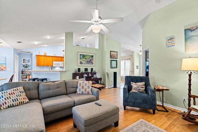 living room featuring light hardwood / wood-style flooring, ceiling fan, high vaulted ceiling, and sink