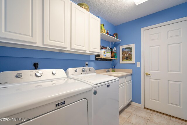 laundry area featuring cabinets, a textured ceiling, washer and dryer, sink, and light tile patterned floors