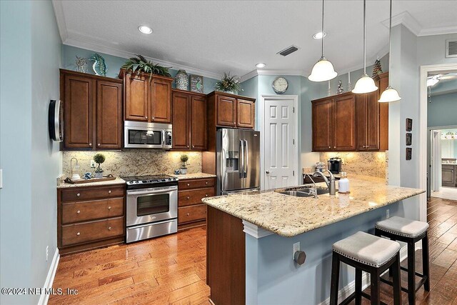 kitchen featuring sink, kitchen peninsula, light hardwood / wood-style flooring, stainless steel appliances, and a kitchen bar