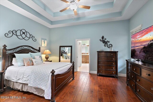 bedroom with ceiling fan, a raised ceiling, connected bathroom, and dark hardwood / wood-style flooring