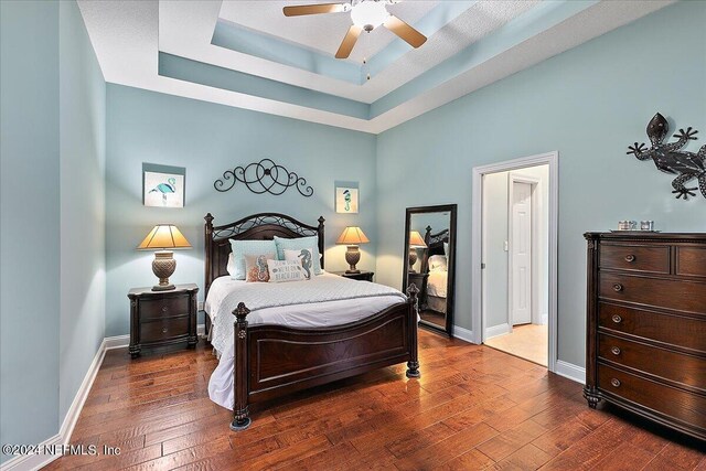 bedroom featuring a tray ceiling, dark wood-type flooring, and ceiling fan