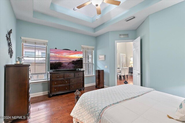 bedroom featuring a textured ceiling, a tray ceiling, dark hardwood / wood-style flooring, and ceiling fan