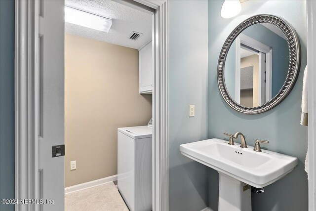 laundry area with light tile patterned floors, a textured ceiling, washer / dryer, cabinets, and sink