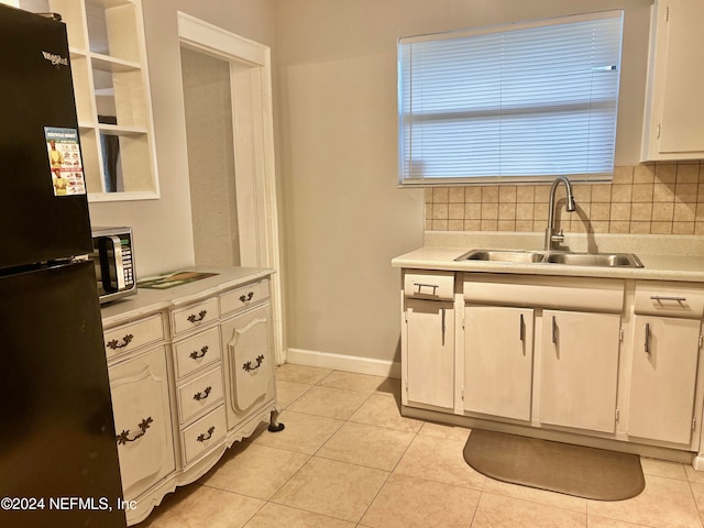 kitchen featuring light tile patterned flooring, white cabinetry, backsplash, sink, and black fridge