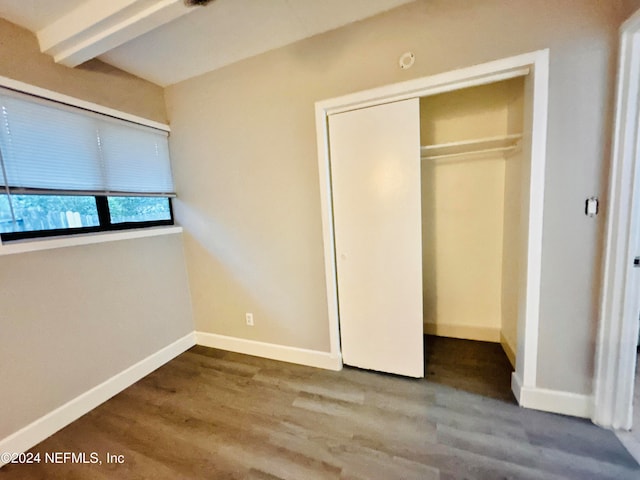 unfurnished bedroom featuring beamed ceiling, a closet, and hardwood / wood-style flooring