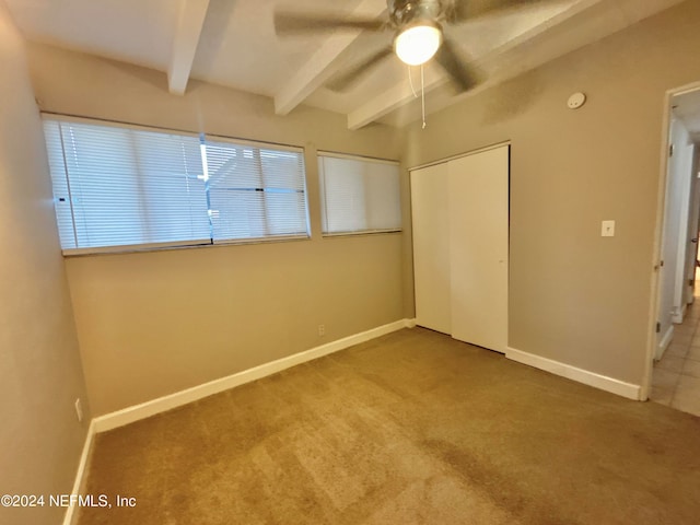 unfurnished bedroom featuring carpet, ceiling fan, beamed ceiling, and a closet