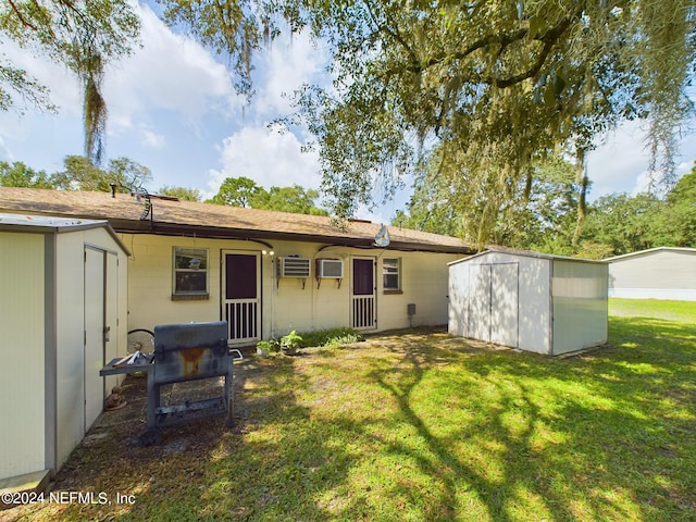 back of house featuring a wall unit AC, concrete block siding, a yard, an outbuilding, and a shed