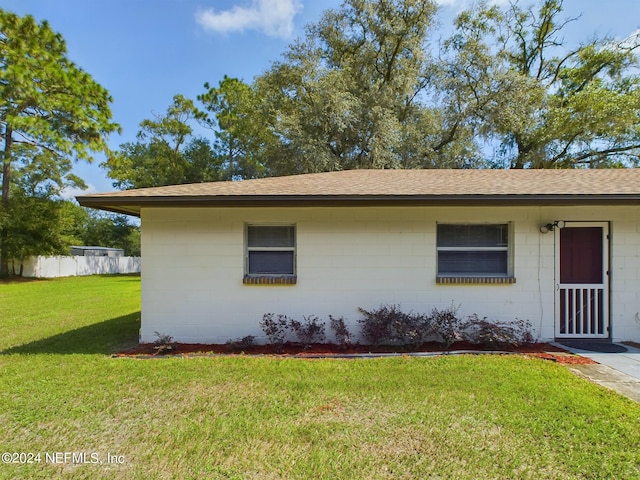 view of front of home featuring fence, a front lawn, a shingled roof, and concrete block siding
