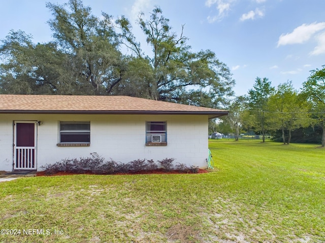 view of home's exterior with a yard, a shingled roof, and concrete block siding