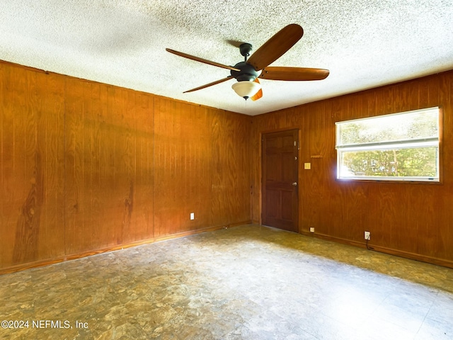 spare room featuring a textured ceiling, ceiling fan, wood walls, and tile patterned floors