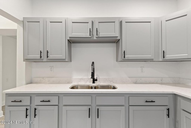 kitchen featuring gray cabinetry, light stone countertops, and sink