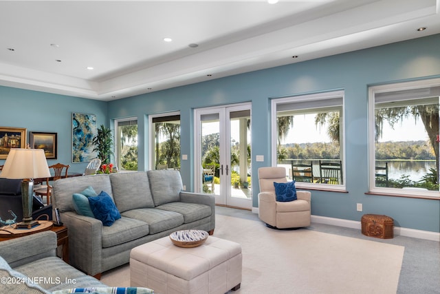 carpeted living room with a wealth of natural light, french doors, and a water view