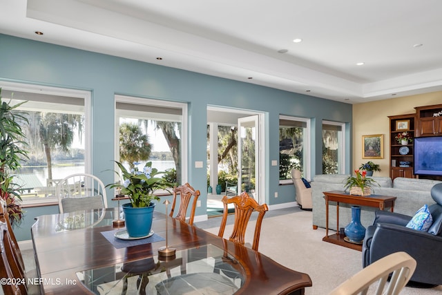 dining room featuring light colored carpet and a raised ceiling