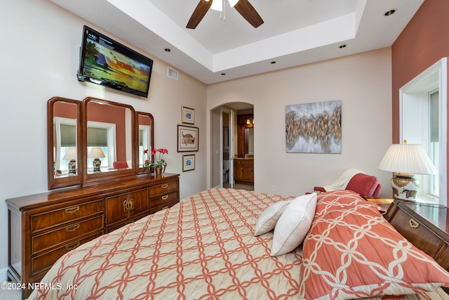 bedroom with connected bathroom, a tray ceiling, and ceiling fan