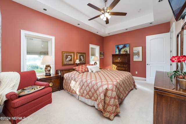 bedroom with light carpet, a tray ceiling, and ceiling fan