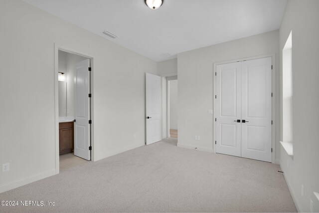 unfurnished bedroom featuring ensuite bath, light colored carpet, and a closet