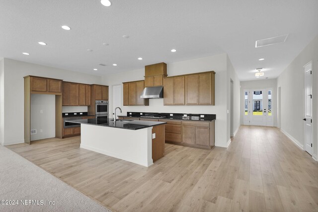 kitchen featuring sink, stainless steel appliances, an island with sink, and light wood-type flooring