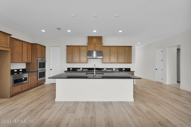 kitchen featuring an island with sink, sink, stainless steel double oven, and light hardwood / wood-style flooring