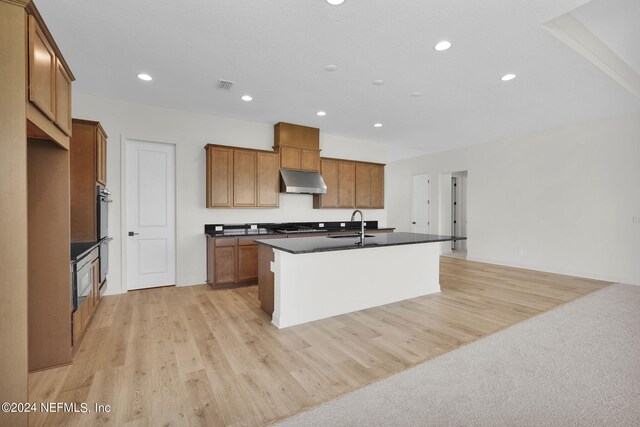 kitchen with stainless steel appliances, sink, a center island with sink, and light hardwood / wood-style flooring