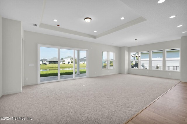 unfurnished living room with an inviting chandelier, a tray ceiling, and light colored carpet