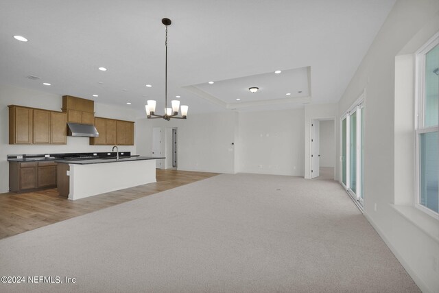 kitchen featuring pendant lighting, a notable chandelier, a tray ceiling, light carpet, and a center island with sink